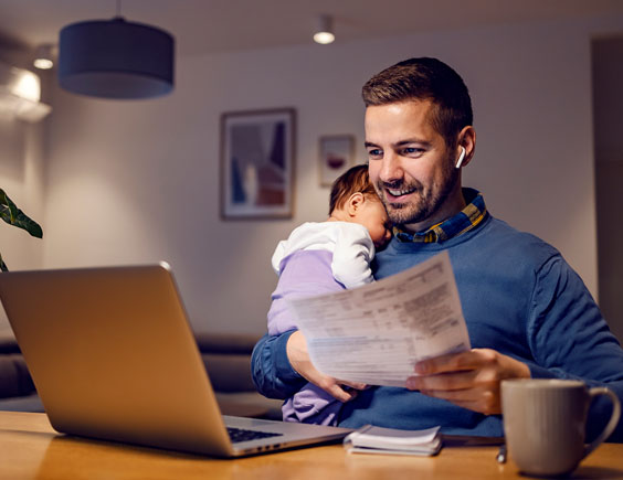 Hombre trabajando con el ordenador, sosteniendo en un brazo a un bebé y en el otro un documento